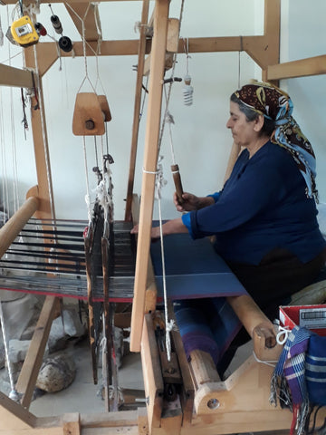 A woman using a traditional Turkish loom to handmake Turkish towels. She is seated and has a fabric covering over her hair.