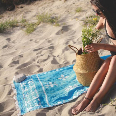 A young woman seated on a Turkish towel at the beach