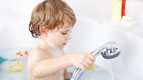 toddler in bath playing water bath game with nozzle