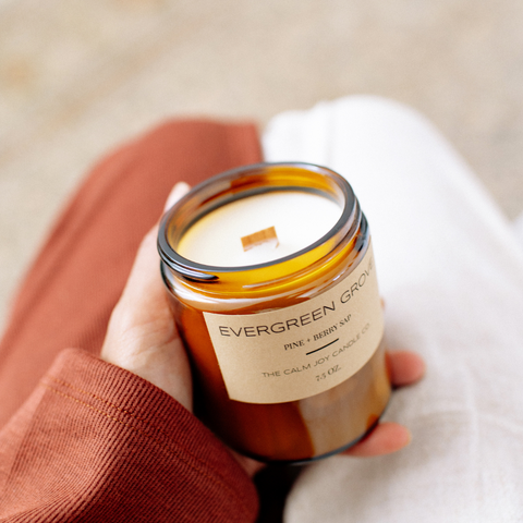 a hand holding an amber glass candle jar labeled and scented with pine and berry sap