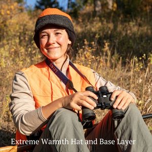 woman sitting outside scouting while hunting wearing orange vest and orange and gray alpaca wool extreme warmth hat