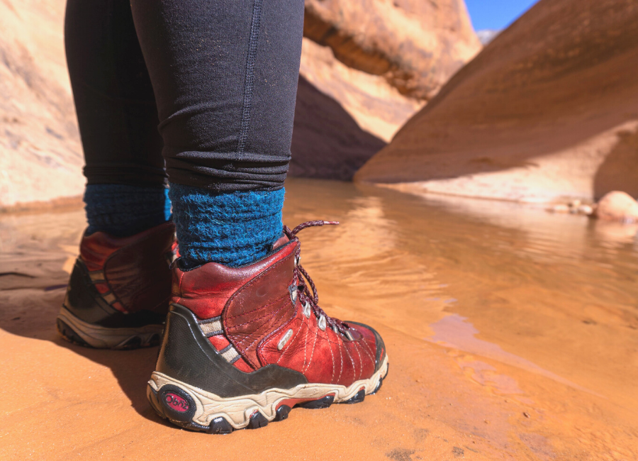 photo of person's feet standing near water in canyonlands wearing red hiking boots and blue alpaca wool wicking and warm adventure socks