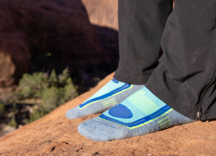 feet standing on a rock wearing blue and green alpaca wool mid crew breathable socks