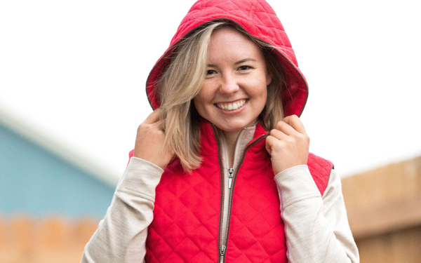 woman smiling holding the hood of her red alpaca wool vest and wearing oatmeal alpaca wool base layer