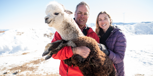 owners of alpacas of montana james and sarah budd smiling holding a baby alpaca