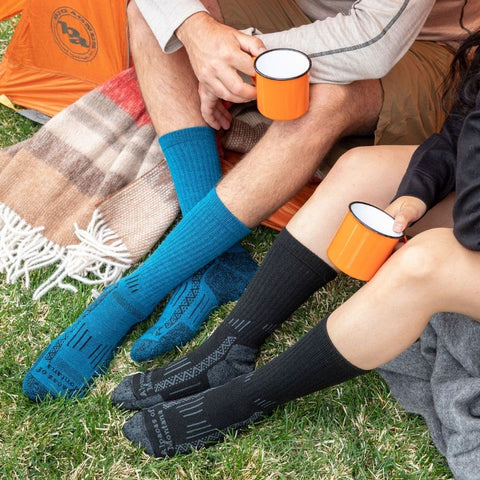 two people sitting with their feet together wearing blue and black warm alpaca wool adventure socks for cold feet