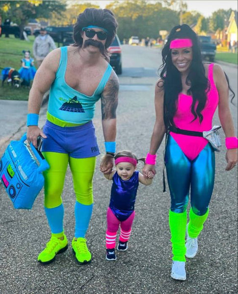 A family dressed in 1980s themed Halloween costumes, featuring neon colored unitards, leggings, headbands, and wristbands.