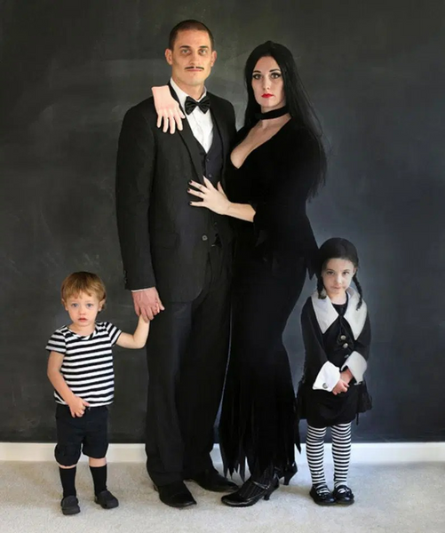 A family dressed in Addams Family Halloween costumes, featuring Morticia Addams, Gomez Addams, Wednesday Addams, and Pugsley Addams.