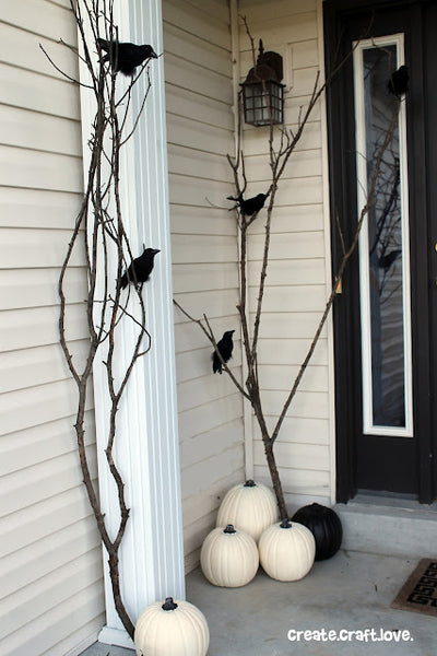 Fake black crows sit perched atop tree branches decorating someone's porch.
