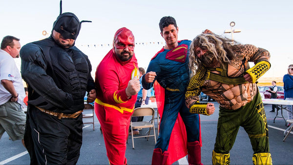A group of men dressed in a Justicce League group Halloween costume, featuring Batman, The Flash, Superman, and Aquaman.