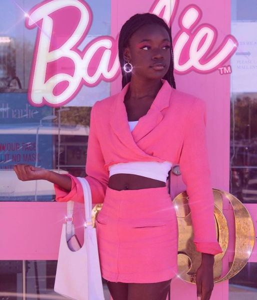 A woman wears a DIY Barbie Halloween costume, featuring a cropped hot pink suit jacket and a matching pink miniskirt.