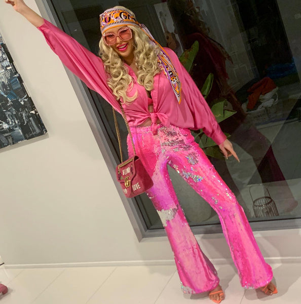 A woman wears a DIY Barbie Halloween costume, featuring a pink silk shirt tied at the front and pink sequined hotpants.