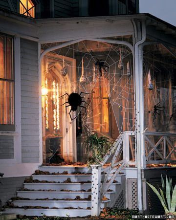 A giant floating spider hangs among giant spider webs on a front porch.