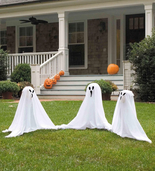 Three ghost decorations sit in the front yard of a house.