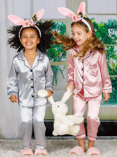 Two young girls wearing silk pajamas, bunny ears, and fluffy slippers.