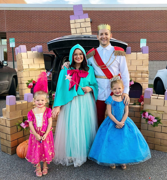 A family dressed in fairy-tale themed Halloween costumes, featuring a Prince, Princess, and a Fairy Godmother.