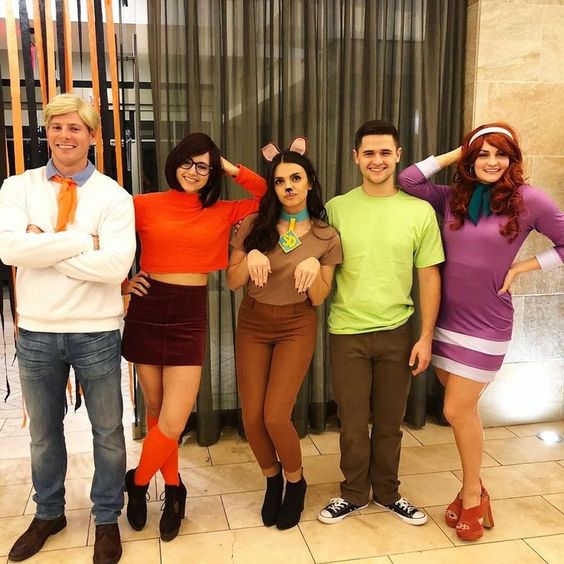 A group of friends dressed as Fred, Velma, Scooby, Shaggy, and Daphne in a Scooby-Doo group Halloween costume.