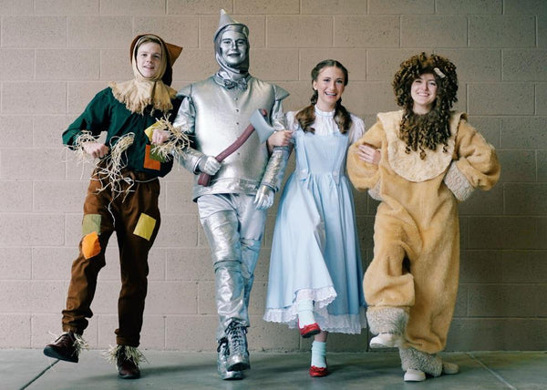 A group of people dressed in a Wizard of Oz group Halloween costume, featuring Scarecrow, Tin Man, Dorothy, and the Cowardly Lion.