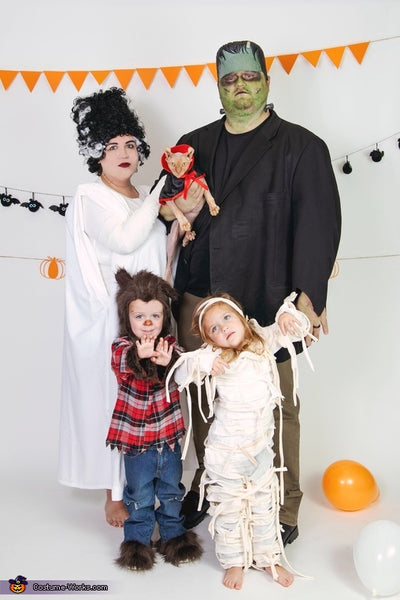 A family dressed in monster-themed Halloween costumes, featuring Frankenstein, the Bride of Frankenstein, a Werewolf, a Mummy, and a Vampire.