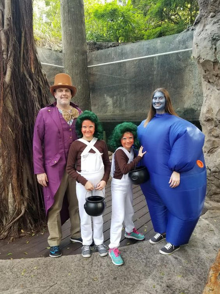 A family dressed in Willy Wonka Halloween costumes, including Willy Wonka, Violet Beauregarde, and two Oompa Loompas.