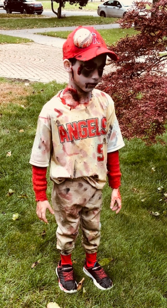 A young boy wearing a baseball uniform speckled in fake blood.