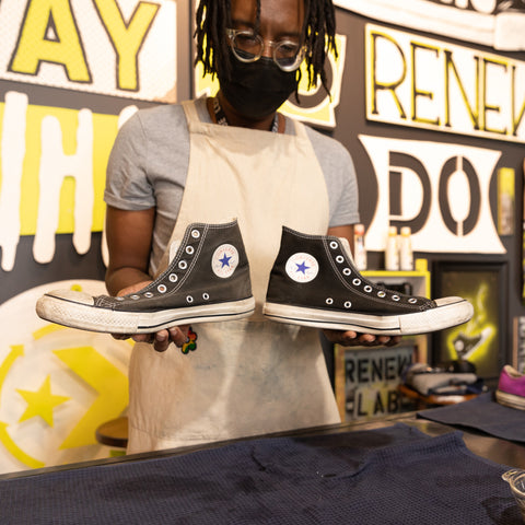 A young man is holding a pair of black Converse Chuck Taylor All Stars