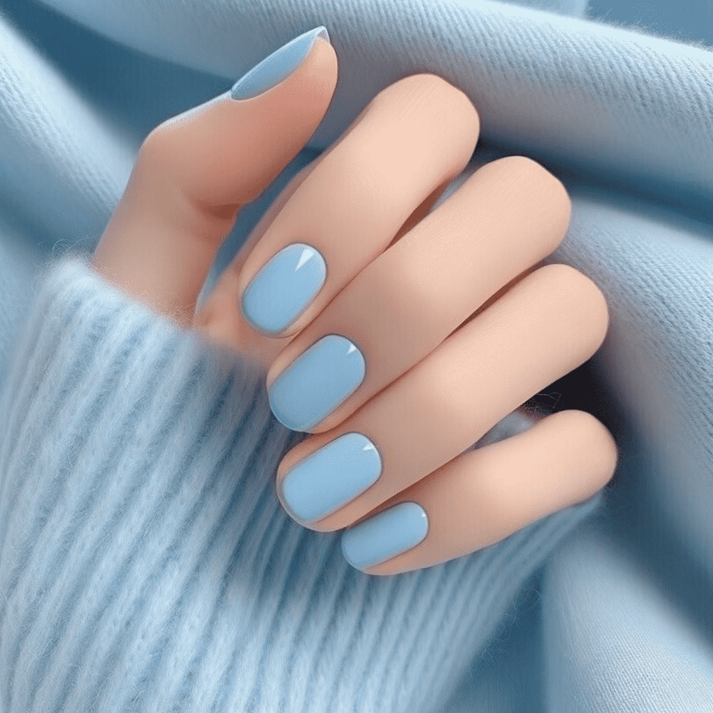 Alt text: A hand with nails painted in a pastel blue color, positioned against a soft, blue fabric background.