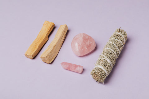 Tools for cleansing your energy. Palo Santo wood, rose quartz and a sage bundle on a pink background. 