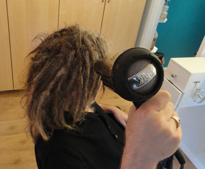 man blow drying dreadlocks with handheld blow dryer in a salon chair