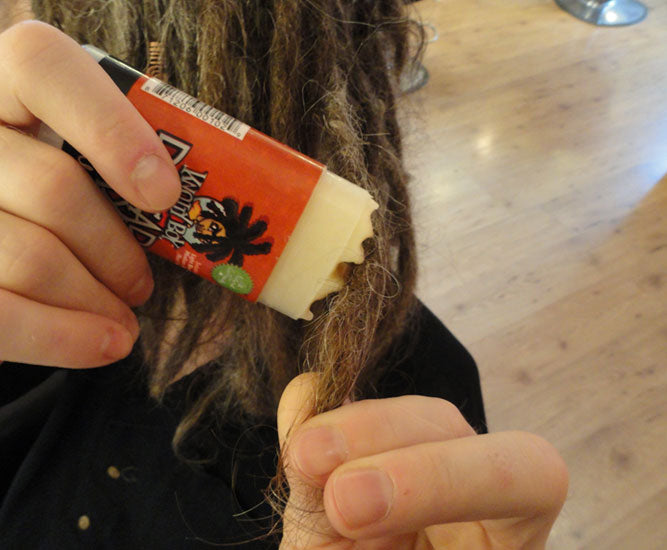 close up of light colour dread wax stick being applied to dreadlocks