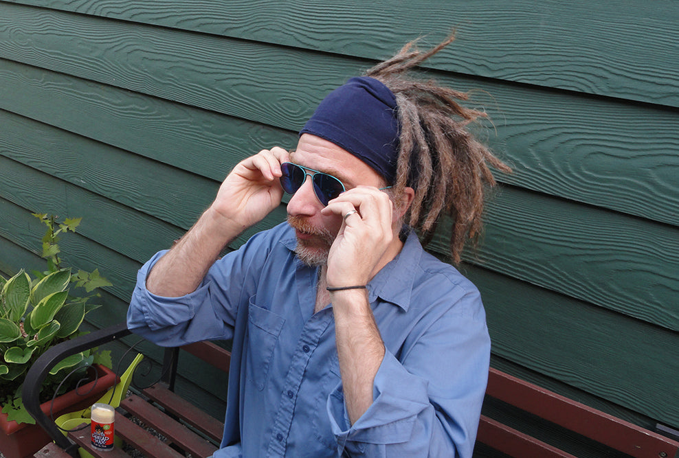 man with blue shirt and blue tinted shades and dark blue dreadlock band adjusting glasses and looking way too serious for what he's doing