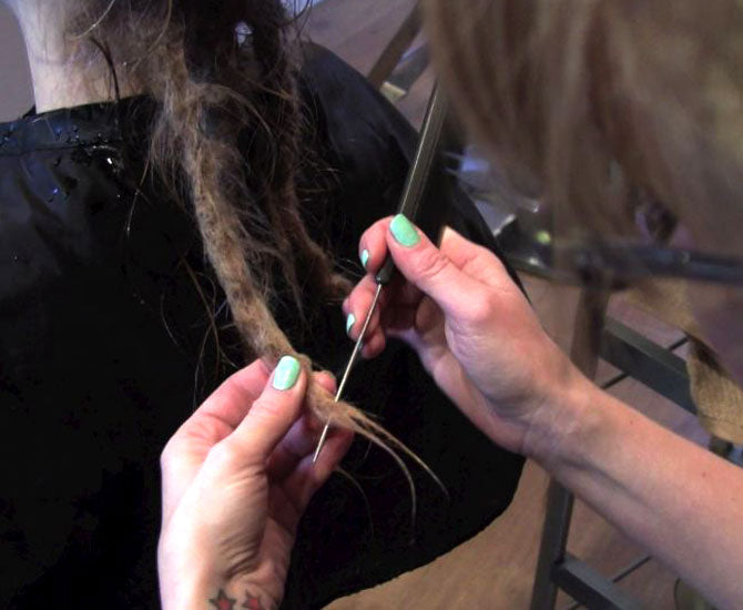 stylist's hands holding tail comb piercing the end of a dreadlock being removed professionally