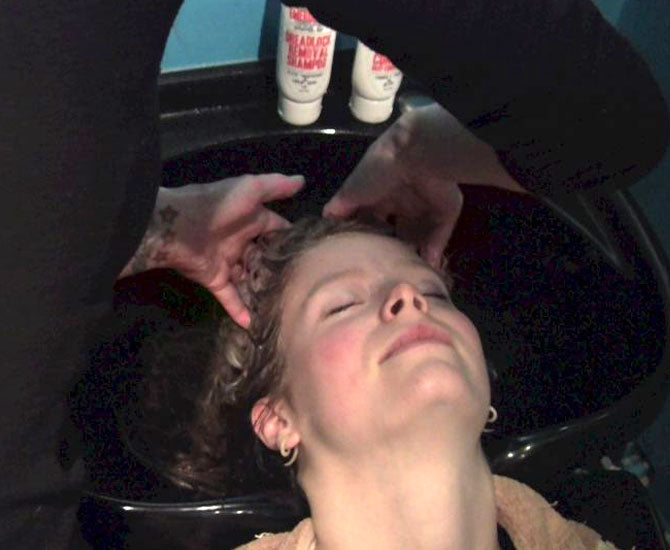 woman with her eyes closed laying her head back in a salon sink having her hair rinsed 