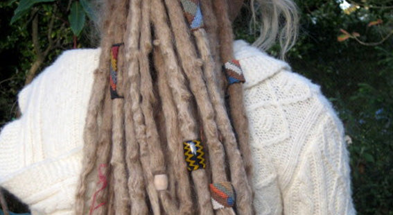 back view of shoulders of person wearing a thick white cable knit sweater with awesome phat blond dreadlocks highly adorned