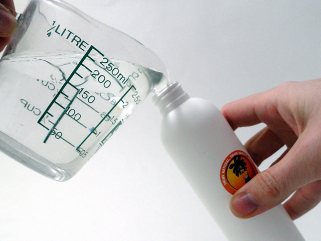 measuring cup pouring clear liquid into a Knotty Boy spritzer bottle