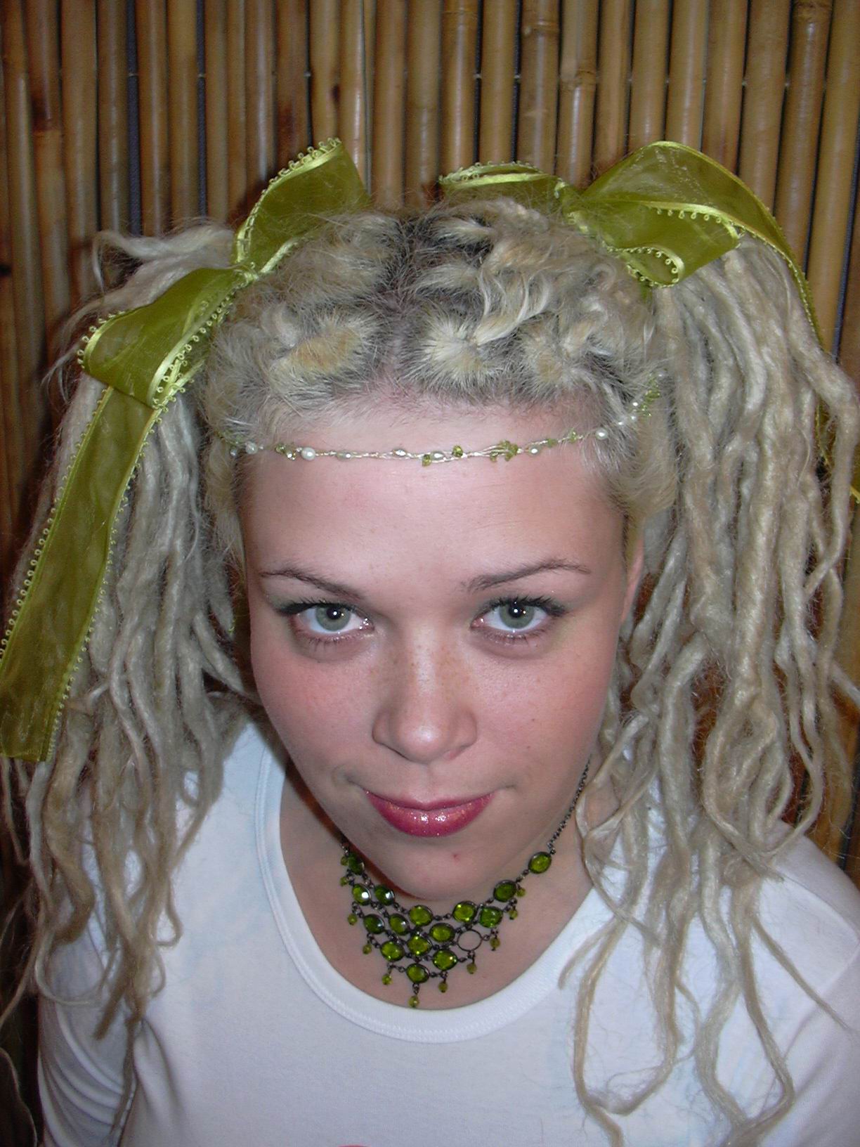 smiling woman with blonde dreadlocks bunched into two parts held together by green ribbons