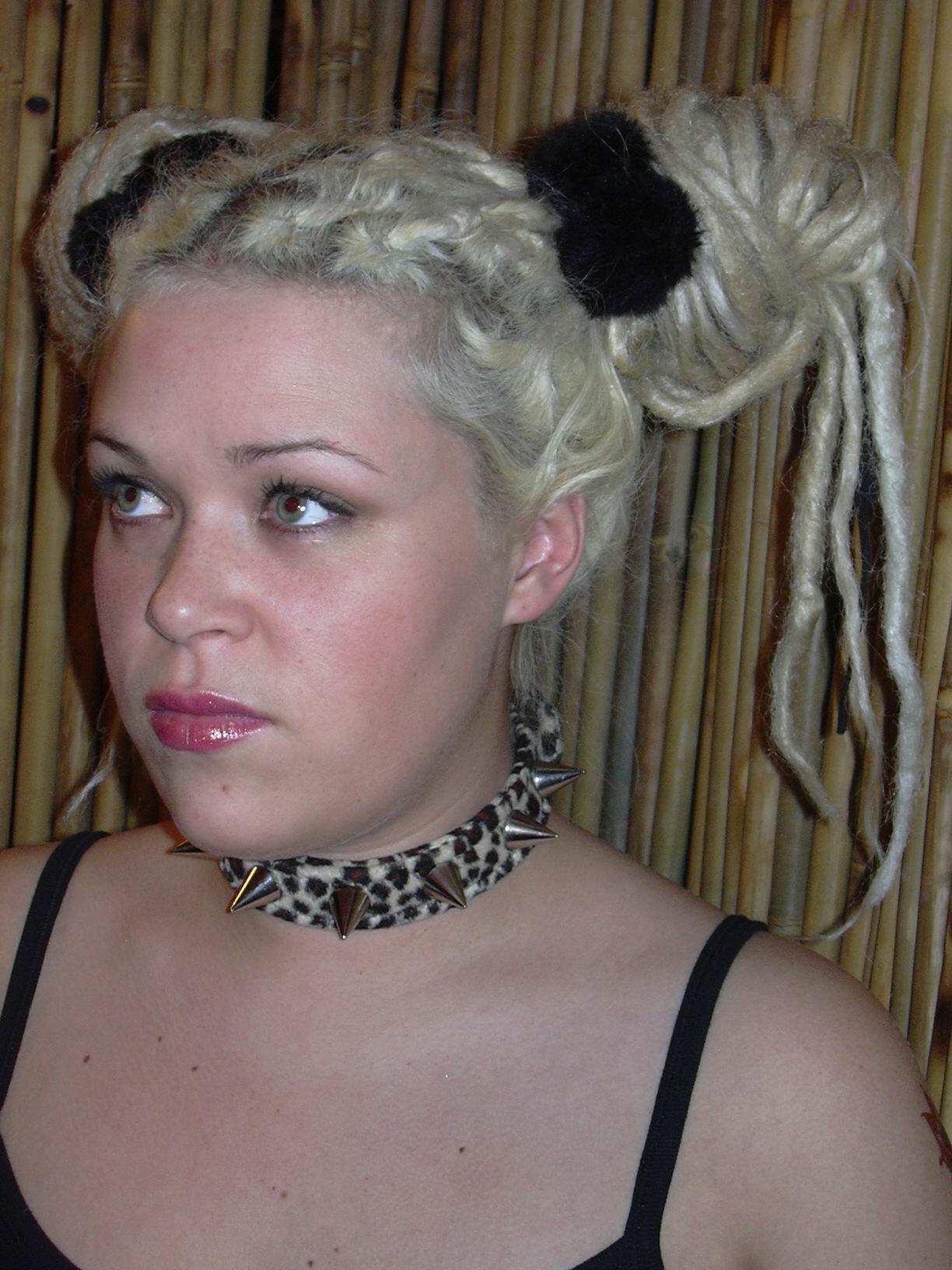 woman looking to the right of camera and upwards wearing spiky collar and blonde dreadlocks in bunches held up by black scrunchies