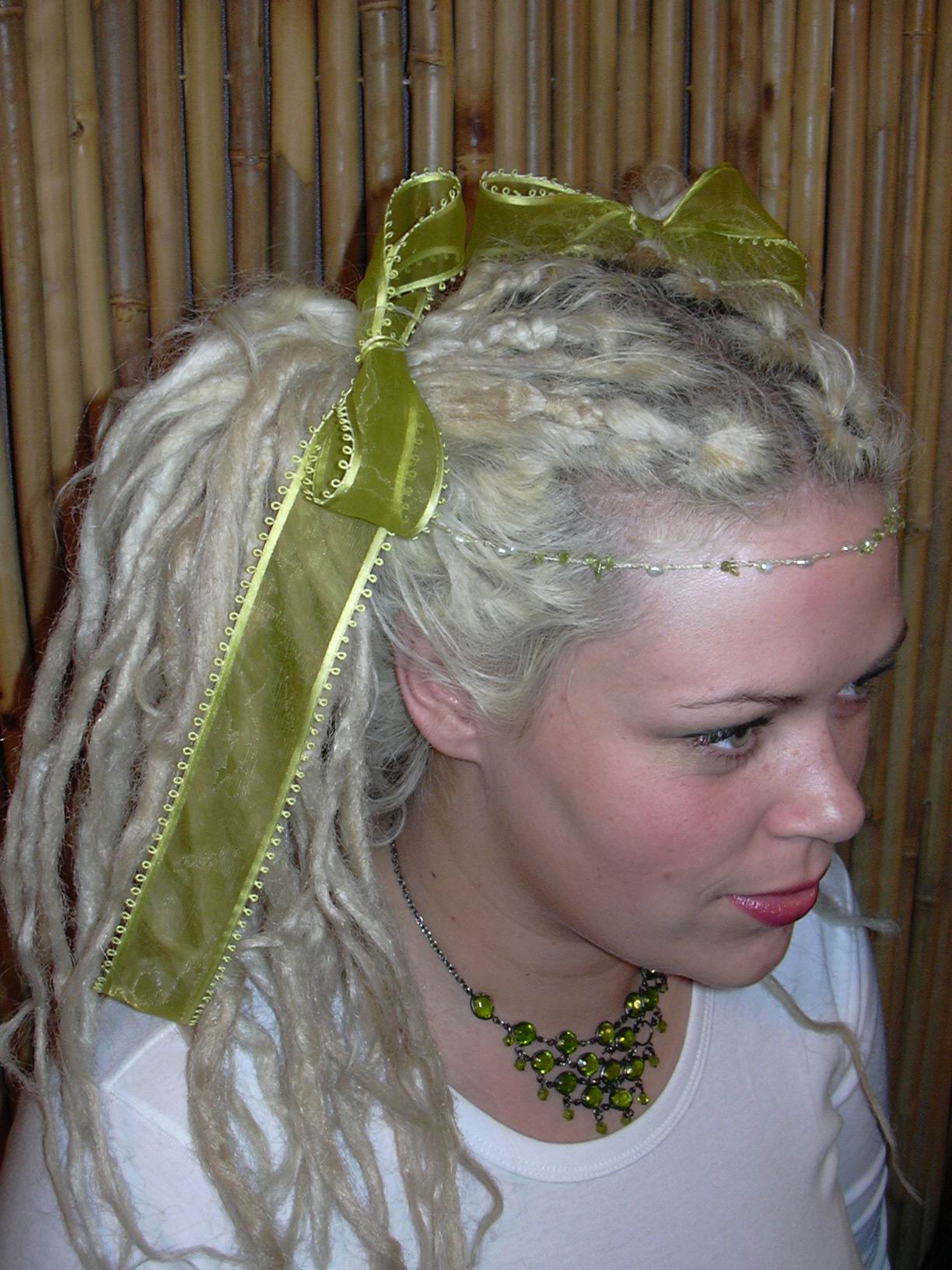 woman lookint to right of camera with bunched pigtailed dreadlocks held together by green ribbons tied in bows