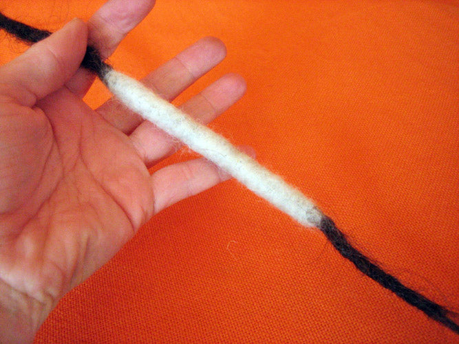 hand holding a dark dreadlock with white wool felting against a deep orange background