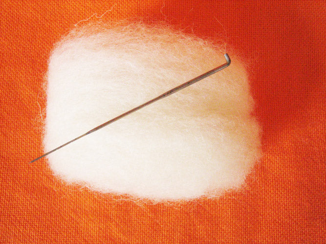 small pile of white wool with roving needle laying on top