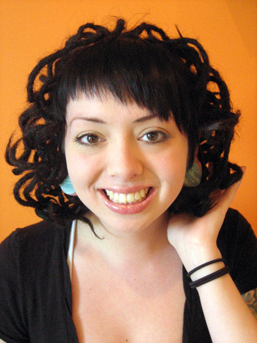 smiling young woman with dark brown bangs and freshly-curled dreadlocks against an orange background