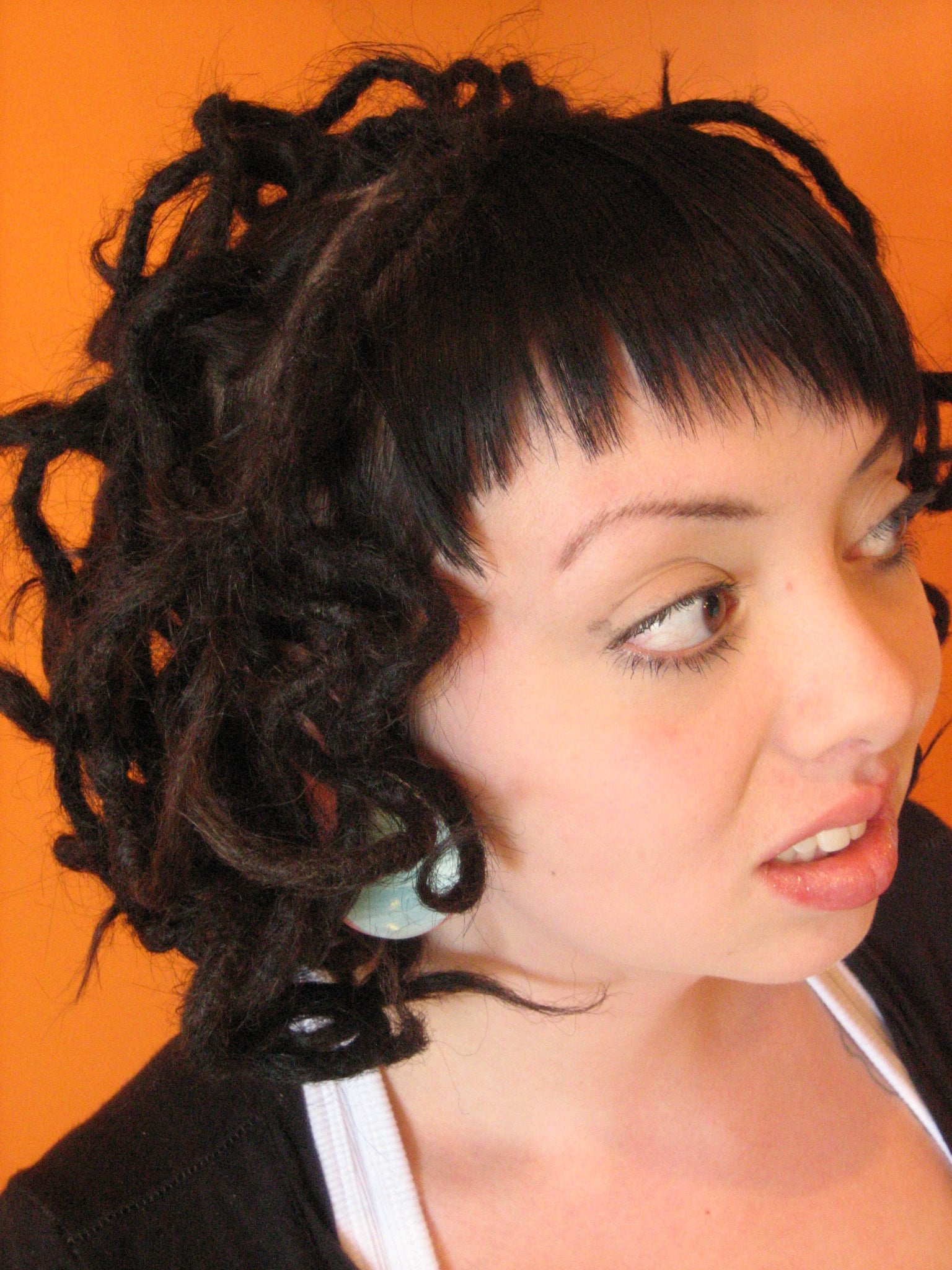 side view of woman against an orange background with curled dark brown dreadlocks