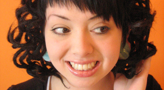 closeup of woman against an orange background with curled dark brown dreadlocks