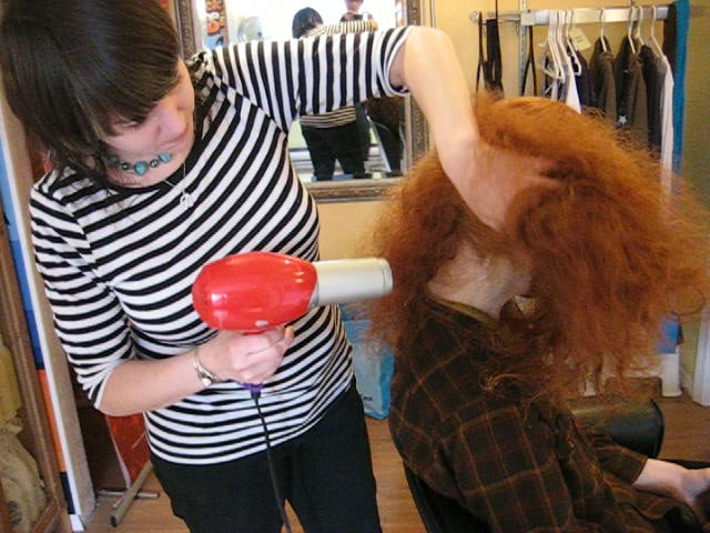 stylist blow drying freshly washed long red hair on model a big fluffy mess