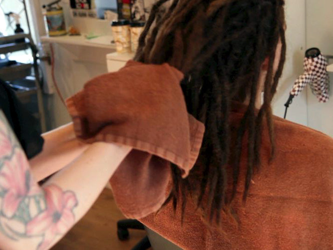 man in salon chair seen from behind with his freshly shampooed dreadlocks being squeezed in a towel