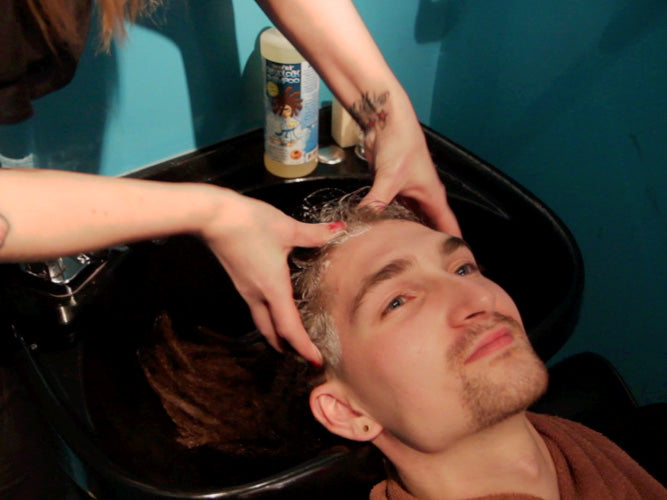 man shot from partially above head back in a salon sink having his dreadlocks shampooed