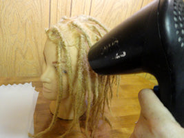 fake model head with overly waxed dreads being blown dry by a hand dryer