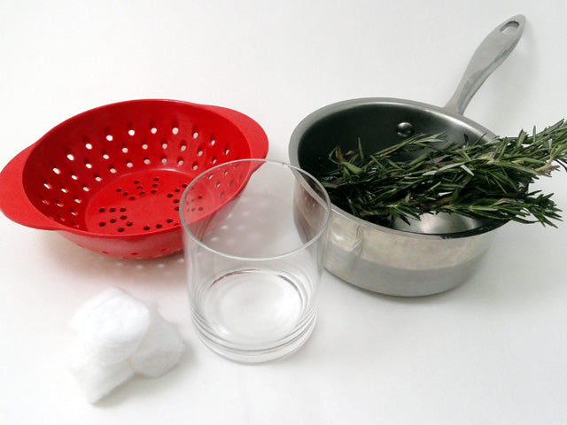 array of necessaries to create this infusion consisting of small red plastic strainer, pile of cotton balls, clear glass, small pot and a small bunch of fresh rosemary