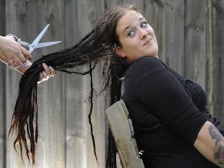 woman with long dreadlocks looking backwards apprehensively as a pair of hands holding scissors and her dreadlocks appears to be preparing to cut them