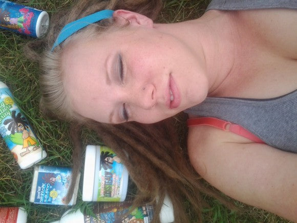 young dreadlocked woman with her eyes closed laying on the grass with a scatter of Knotty Boy products around her head